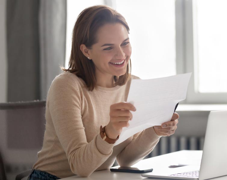 Une femme souriante regarde des documents à son bureau.