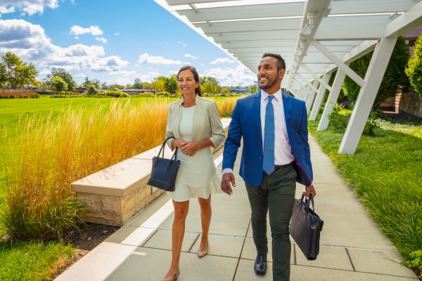 Business woman walking with business man on corporate campus.