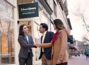 Une représentante en services financiers Edward Jones serre la main d’une cliente à l’extérieur d’un bureau pendant qu’un client les regarde.