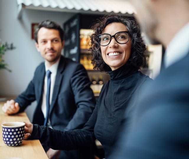 ejd-db-1 Une femme et un homme souriants, assis à une table, discutent avec un autre homme.