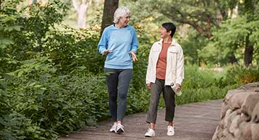 Two women walking briskly in park, conversing