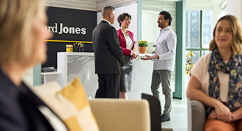 Women sitting and have discussion with a small group standing in the background talking in an Edward Jones office.