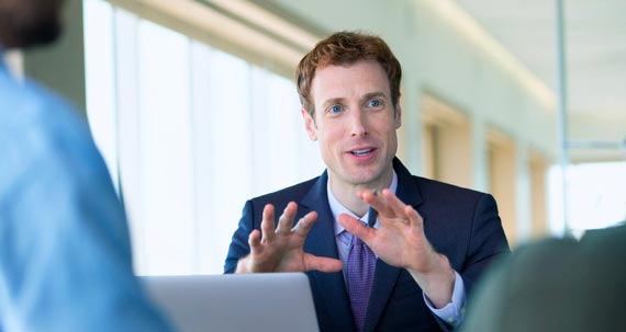 A man behind a laptop speaking to two other people.