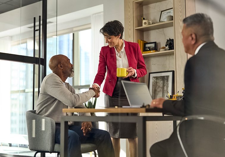 Woman shaking hand with client while a man watching on.